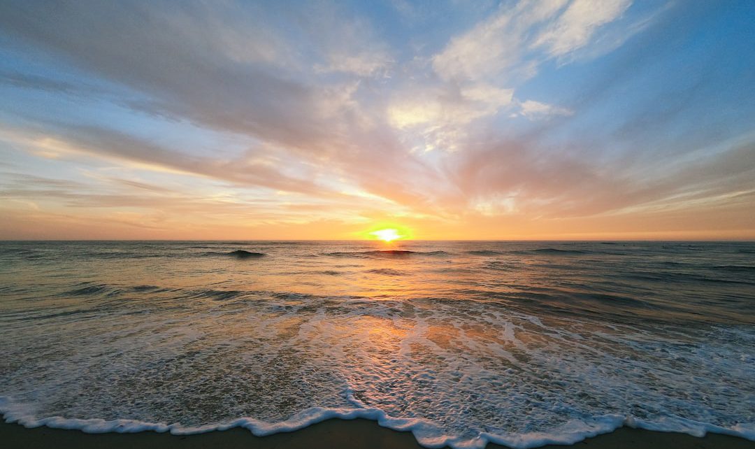 A serene sunset over a calm ocean with gentle waves lapping at the shore.