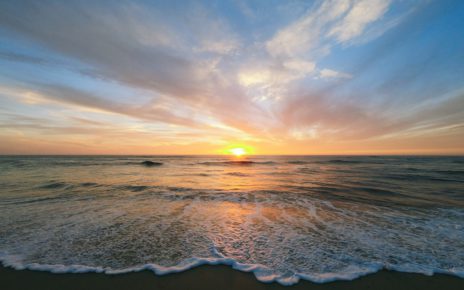 A serene sunset over a calm ocean with gentle waves lapping at the shore.